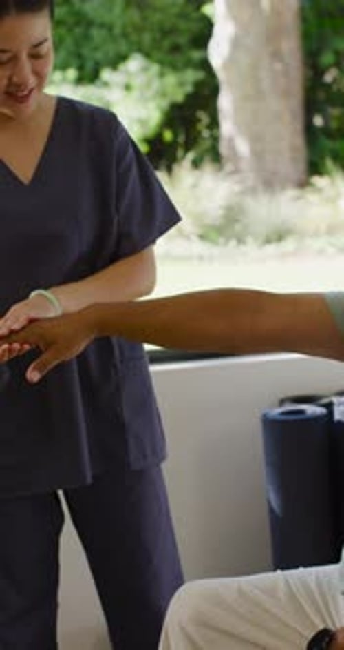 Vídeo vertical: paciente diversificado e enfermeira asiática avaliando o pulso enquanto o paciente estende o braço na clínica