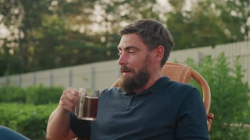 Gardener Stirring Coffee in Wicker Chair at Sunset Garden Break