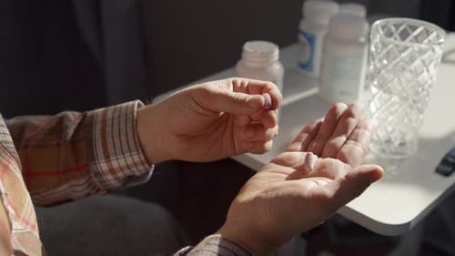 Man Holding Pills Beside Medication Bottles in Home