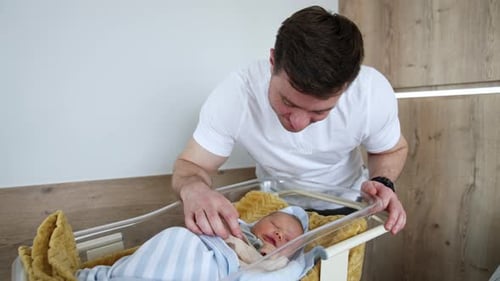 Man Tenderly Watching Over Newborn Baby in Bassinet