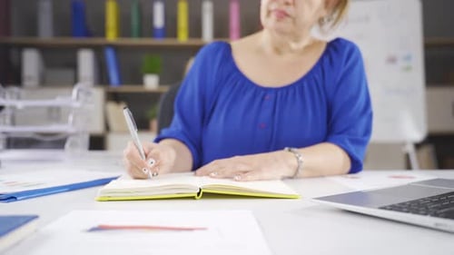 Woman Writes in Notebook at Desk in Office