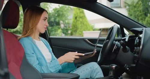Retrato de una mujer joven que trabaja y usa un ordenador portátil mientras está sentada en el coche, celebrando un seminario