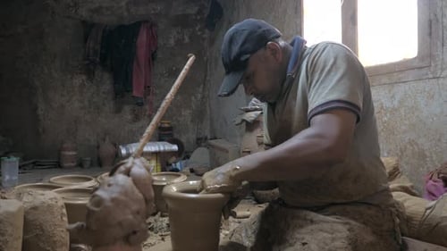 Side view of potter making and shaping clay vessel rotating on potters wheel.
