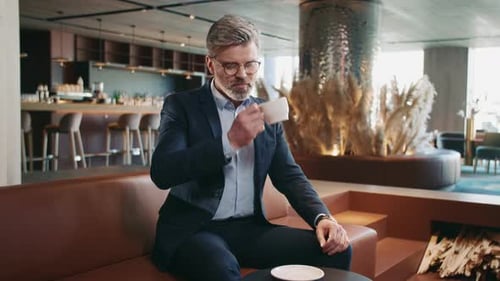 Welldressed Businessman Sitting at Table in Cafe Drinking Coffee Looking at Watch Shot of
