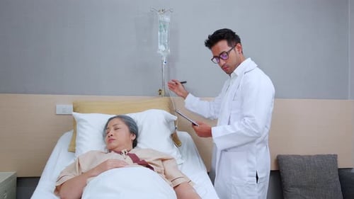 Asian doctor check saline and check patient elderly while asleep on bed at hospital ward.