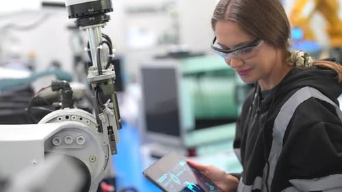 Une
technicienne programme un bras robotique avec une tablette numérique et un robot d'assemblage dans une usine. Appren