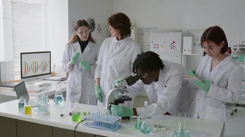 Afroamerikanischer Student benutzt Mikroskop mit seinen Klassenkameraden und seinem Lehrer im Labor