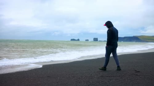 Man Walking Alone At The Famous Black Sand Beach Of Reynisfjara In Southern Iceland. wide shot