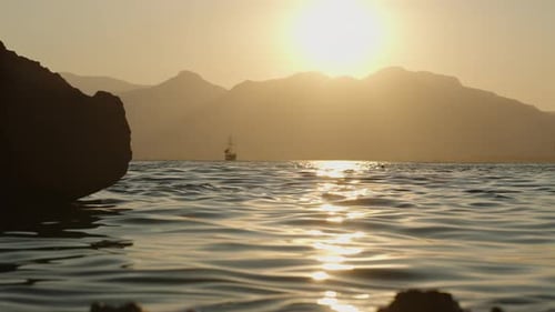 A Serene Sunset Over the Sea with Silhouetted Mountains in the Distance, a Small Boat Sailing