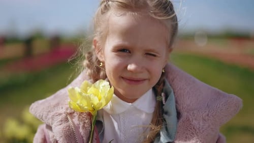 A Cheerful Young Girl Happily Holding a Bright Yellow Flower in a Beautiful Tulip Field of Colors