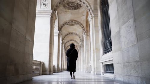 Mulher caminhando pelos arcos do Museu do Louvre em Paris, França. - Follow Shot, ângulo baixo