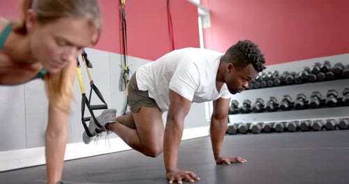 Fit young Caucasian woman and African American man doing mountain climbers at the gym