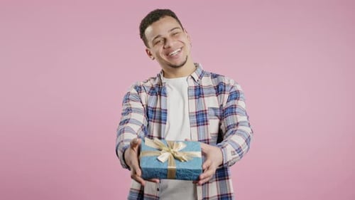 Young Man Giving Gift to Camera on Pink Background