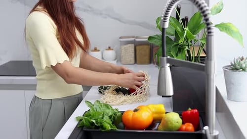 Una joven saca verduras y frutas orgánicas de una bolsa reutilizable en la cocina moderna