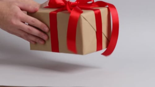 Hands Placing a Wrapped Gift with Red Ribbon