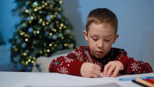 Young Boy Writes Letter near Christmas Tree at Night