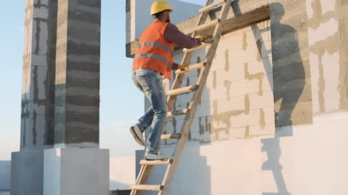 Construction worker climbs ladder to inspect building structure at sunset