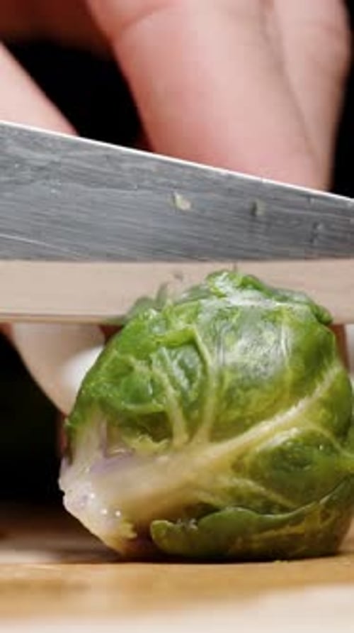 Vertical video. A close-up of a woman cutting a Brussels sprout in half, with other sliced Brussels