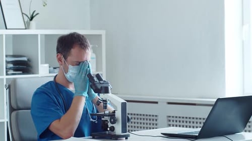 Medical Professional Using Microscope Looks Worried