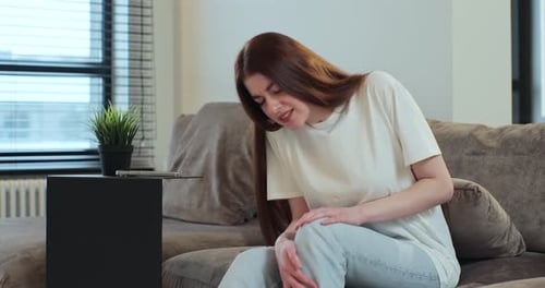Young Woman Rubbing Knee in Pain on Couch