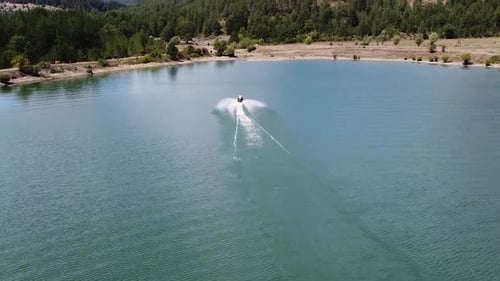 Man has fun on a jet ski on a lake surrounded by pine forest, Albania
