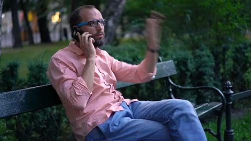 Angry, Unhappy Man Talking on Cellphone, Waiting for Someone at Park 30s