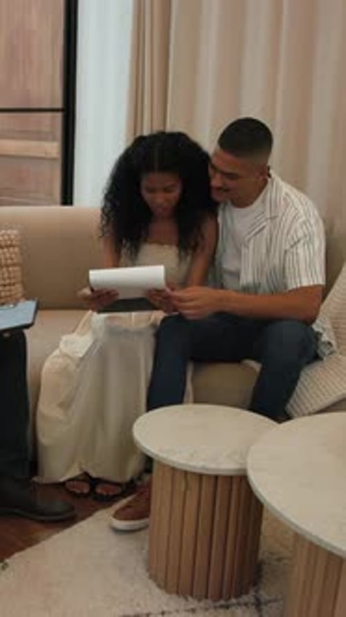 Vidéo verticale : réception d'une tablette, couple en train de réviser des documents et de signer sur le canapé pour finaliser les formalités