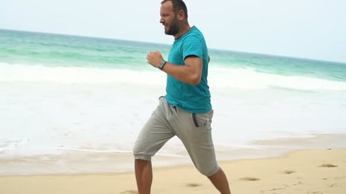 Young man jogging on a tropical beach in super slow motion toning his shape