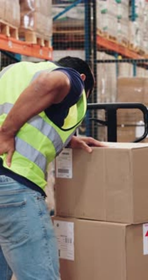 Boxes, supply chain and man in warehouse with back pain, injury or accident with orders