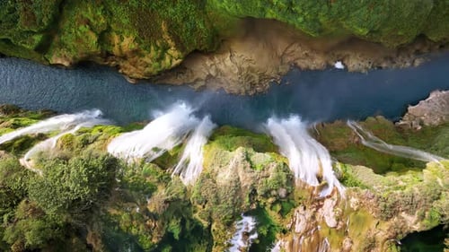 Aerial drone view of several powerful waterfalls dropping into a narrow canyon with green moss and r