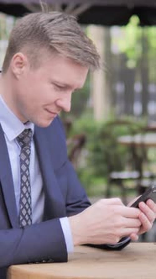 Young Man in Suit Types on Smartphone Outdoors
