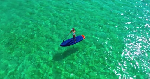 Aerial View of Woman in White Swimsuite Standing on Sup Board with Paddle on Crystal Turquoise Water