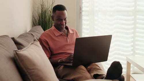 Man Working on Laptop While Relaxing on Couch