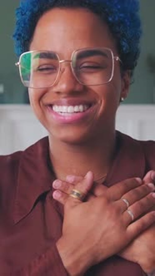 Une personne joyeuse aux cheveux bleus sourit brillamment à l'intérieur pendant la journée