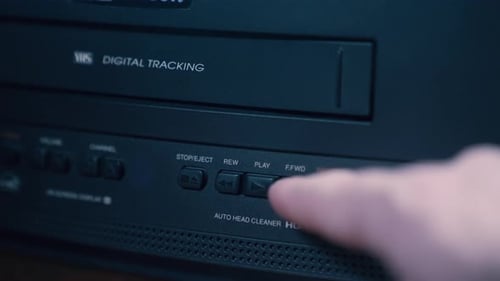Finger presses play button on vintage VHS player