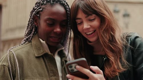 Close up of happy women using a smartphone standing outdoors and laughing
