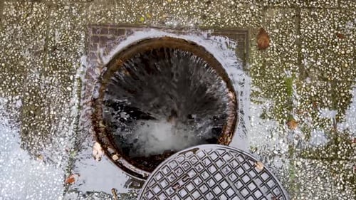 Stream of water flowing down an open sewer grate, after heavy rain that flooded the path.