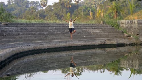 fille faisant la pose d'un arbre vrhsasana, double réflexion d'image dans de l'eau calme sur des marches d'une lame