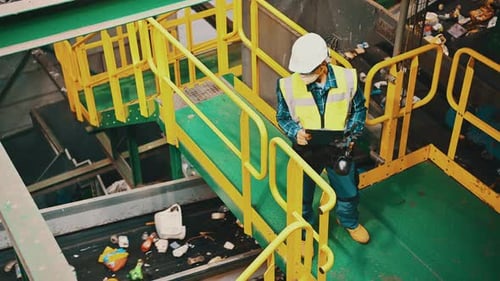 Worker Inspecting Waste on Conveyor Belt at Recycling Plant