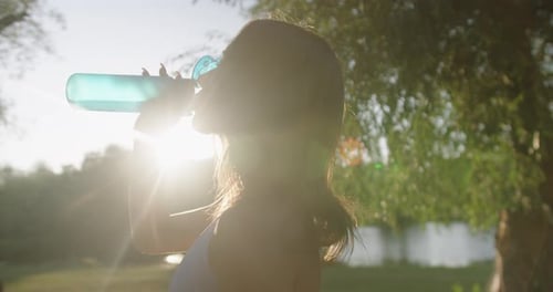 Woman Drinks Water After Workout in Golden Sunlight