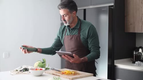 Man in Kitchen Preparing Vegetables with a Tablet