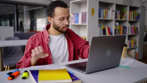 Agréable étudiant afro-américain tapant du texte sur un ordinateur portable travaillant sur une thèse ou un nouveau projet dans la bibliothèque
