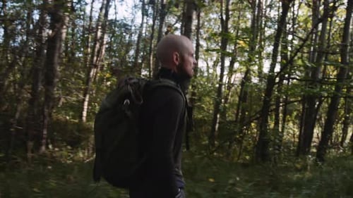Side View of a Man Tourist with Backpack Hiking in the Forest