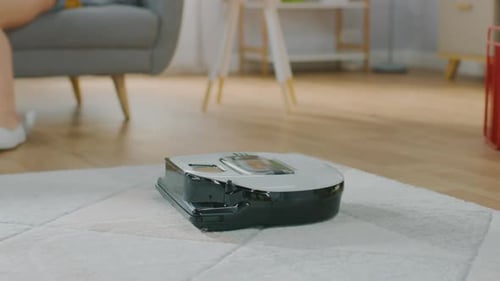 Close Up Shot of a Smart Robot Vacuum Cleaner Sucking Up Dust from a Carpet. Beautiful Couple is Si