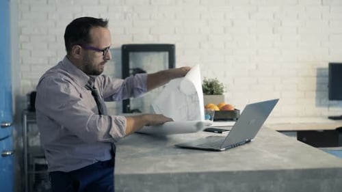 Man reviewing blueprint at kitchen island with laptop
