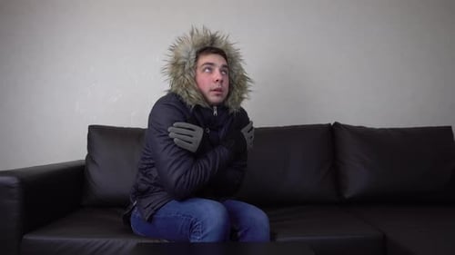 Un jeune homme est assis à la maison dans une veste d'hiver et essaie de rester au chaud
