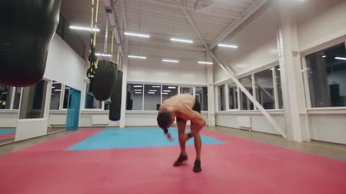 Bodybuilder with a Naked Torso is Training in the Gym and Doing a Back Flip and Clenching His Fists