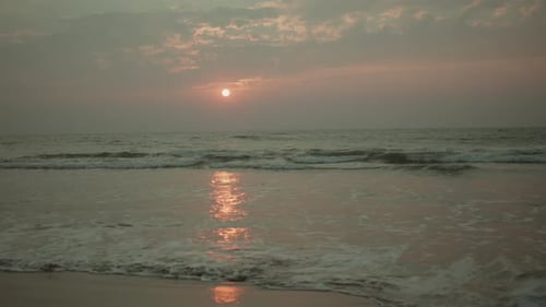 Golden hour sunset over beach with gentle waves rolling in at coastline view