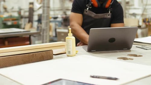 Male Carpenter Working At Laptop In Workshop