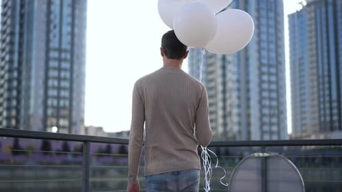 Young Adult Man Holding Balloons on Balcony